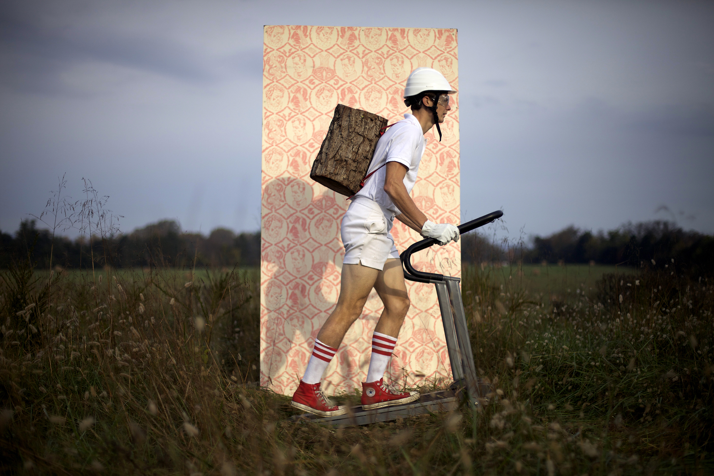 A photograph of a person walking on a treadmill in a field while carrying a log on his back