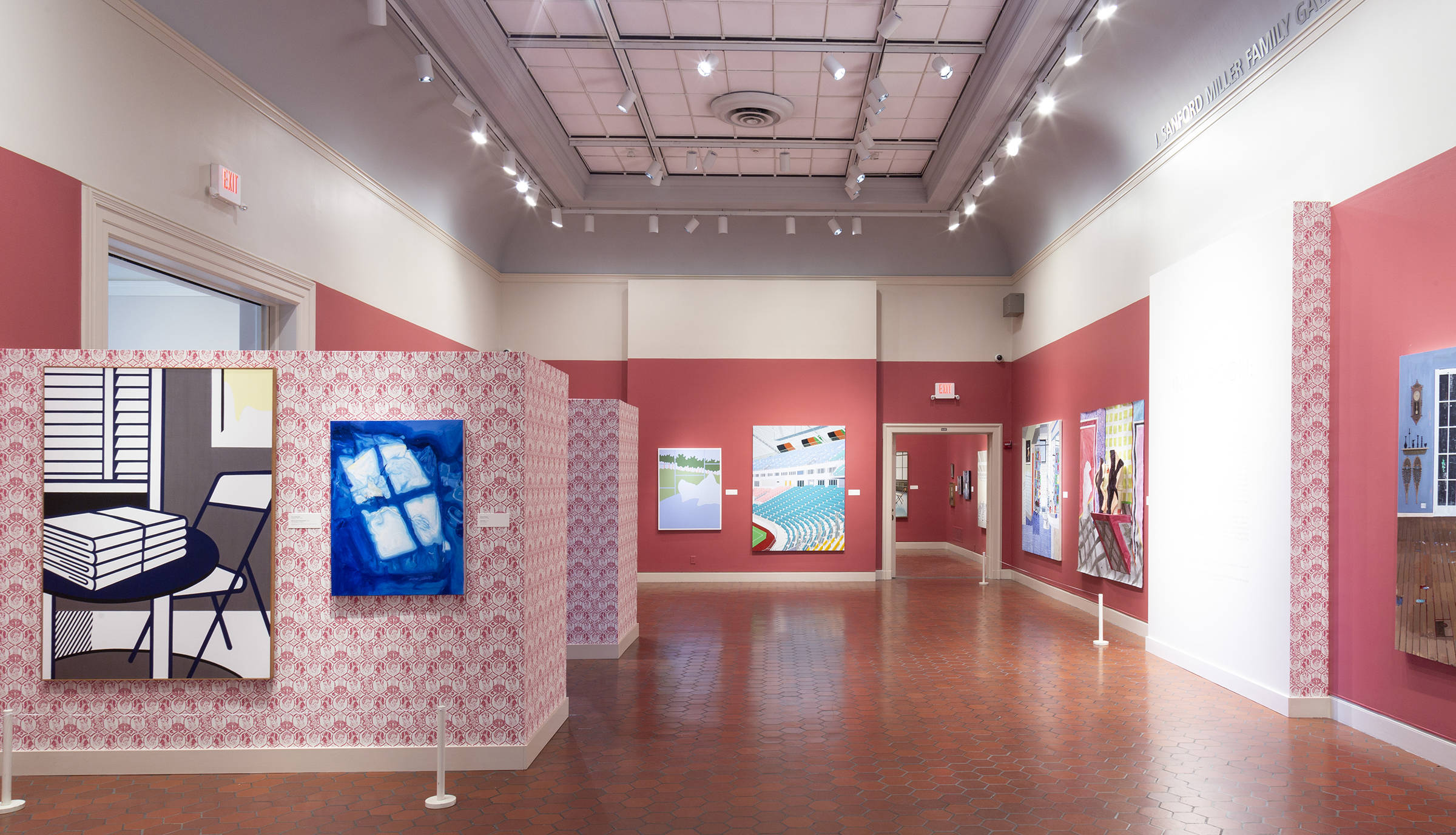 A photograph of an art exhibition in a gallery with lots of paintings and pink patterned wallpaper