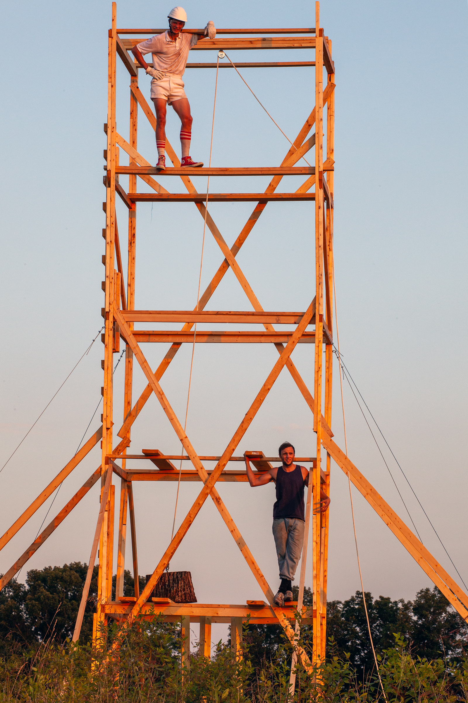 A photograph of two people standing on a wooden scaffolding at sunset
