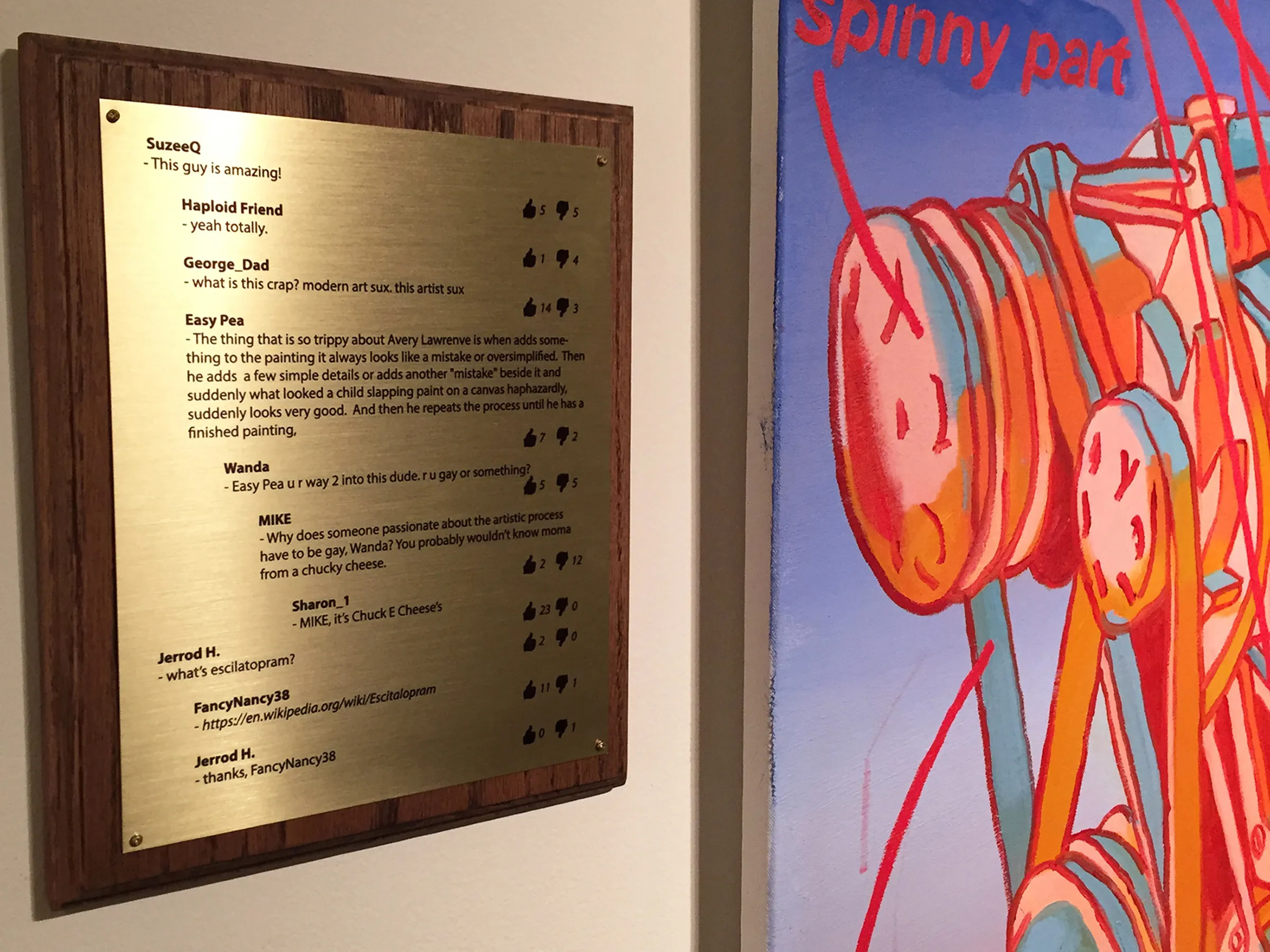 A wood and metal plaque hanging on a wall next to a colorful painting.