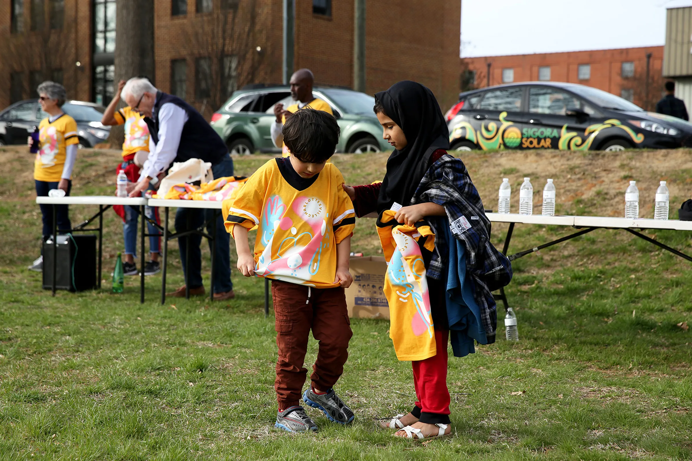 Two children try on matching yellow soccer jerseys while standing on a grassy field.