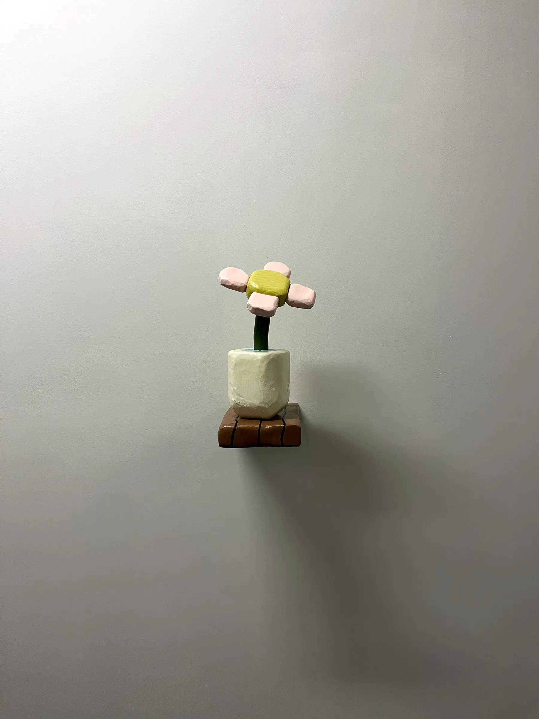 A photograph of a wooden sculpture that looks like a flower in a vase, resting on a short wooden plank.
