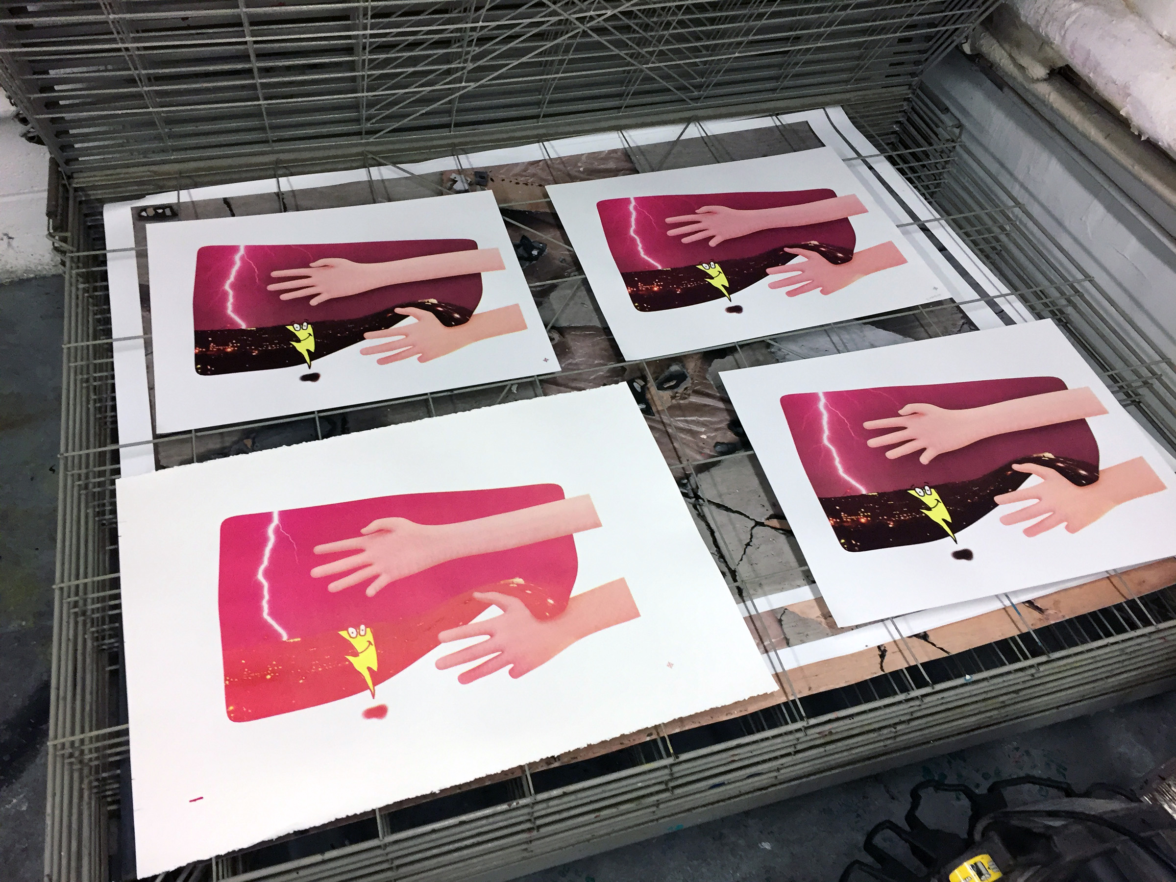 A photograph of four screen prints in a metal drying rack.